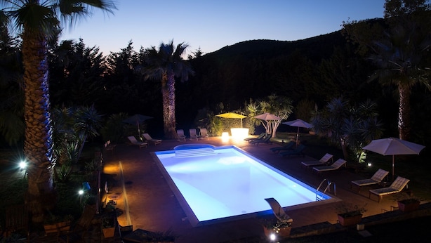 Une piscine entourée de chaises longues et de parasols, bordée de palmiers et avec une montagne en toile de fond.