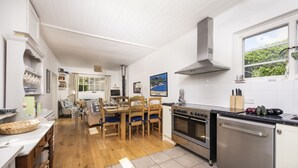 Eine Küche mit Holzboden, weißen Schränken, einem Herd, Backofen und Geschirrspüler. Es gibt eine Essecke mit Tisch und Stühlen.