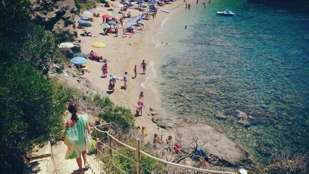 A beach with clear water, a staircase leading down to the shore, and people relaxing under umbrellas. - Apartment surrounded by tranquility with beautiful sea view (Capoliveri)