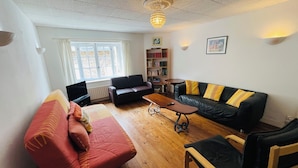 Ein Wohnzimmer mit einem roten Sofa, einem schwarzen Ledersofa und einem Couchtisch aus Holz. Es gibt ein Bücherregal und eine Chandelieber.