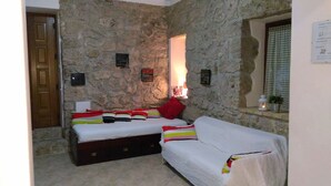 A room with stone walls, a bed with colorful bedding, a small window with a view, and a door.