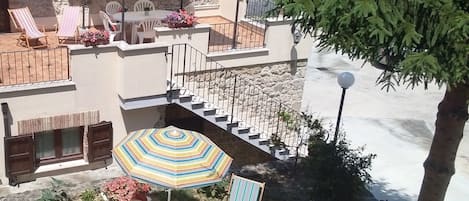 Een terras met buitenmeubilair, een gestreepte parasol en uitzicht op zee.