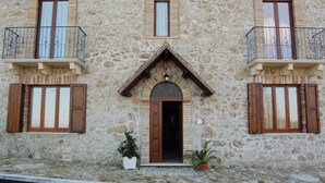 A stone building with a central entrance, two balconies with metal railings, and wooden shutters.