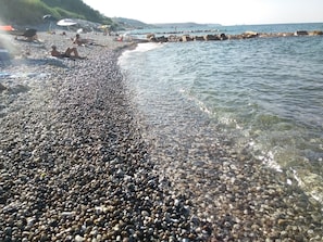 Una playa de guijarros con agua cristalina y un litoral rocoso.