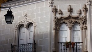 Une façade d’immeuble ornée d’arcs au-dessus des fenêtres, un balcon avec une balustrade en fer forgé et une lanterne suspendue.
