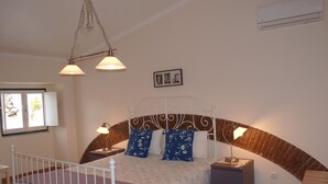 Une chambre à coucher comprenant un lit, des tables de chevet, un luminaire suspendu, un appareil de climatisation et une fenêtre donnant sur un paysage.
