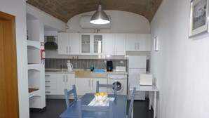 Une cuisine moderne avec des armoires blanches, un four encastré et un évier. On y trouve une table à manger avec des chaises bleues et une petite table recouverte d’une nappe blanche.