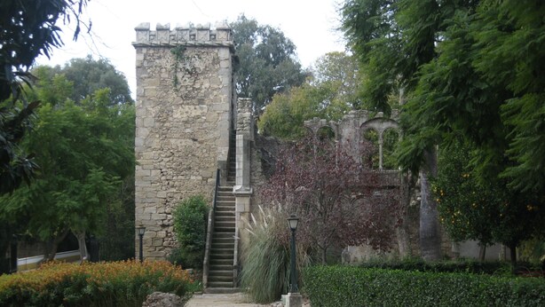 Une tour de pierre, avec un escalier menant à son sommet, entourée de verdure et d’une haie.