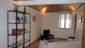 Un salon avec un canapé blanc, une table basse en verre, une bibliothèque, un téléviseur et une fenêtre avec des rideaux.