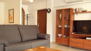 A living room with a grey sofa, wooden cabinet with dishes, a wooden coffee table, and a flat-screen TV. - Front Line 4th floor La Goleta Apt Overlooking Benidorm Island And Levante Beach (Benidorm)