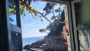 Vista marítima des d'una finestra amb una platja rocosa, gent i barques.
