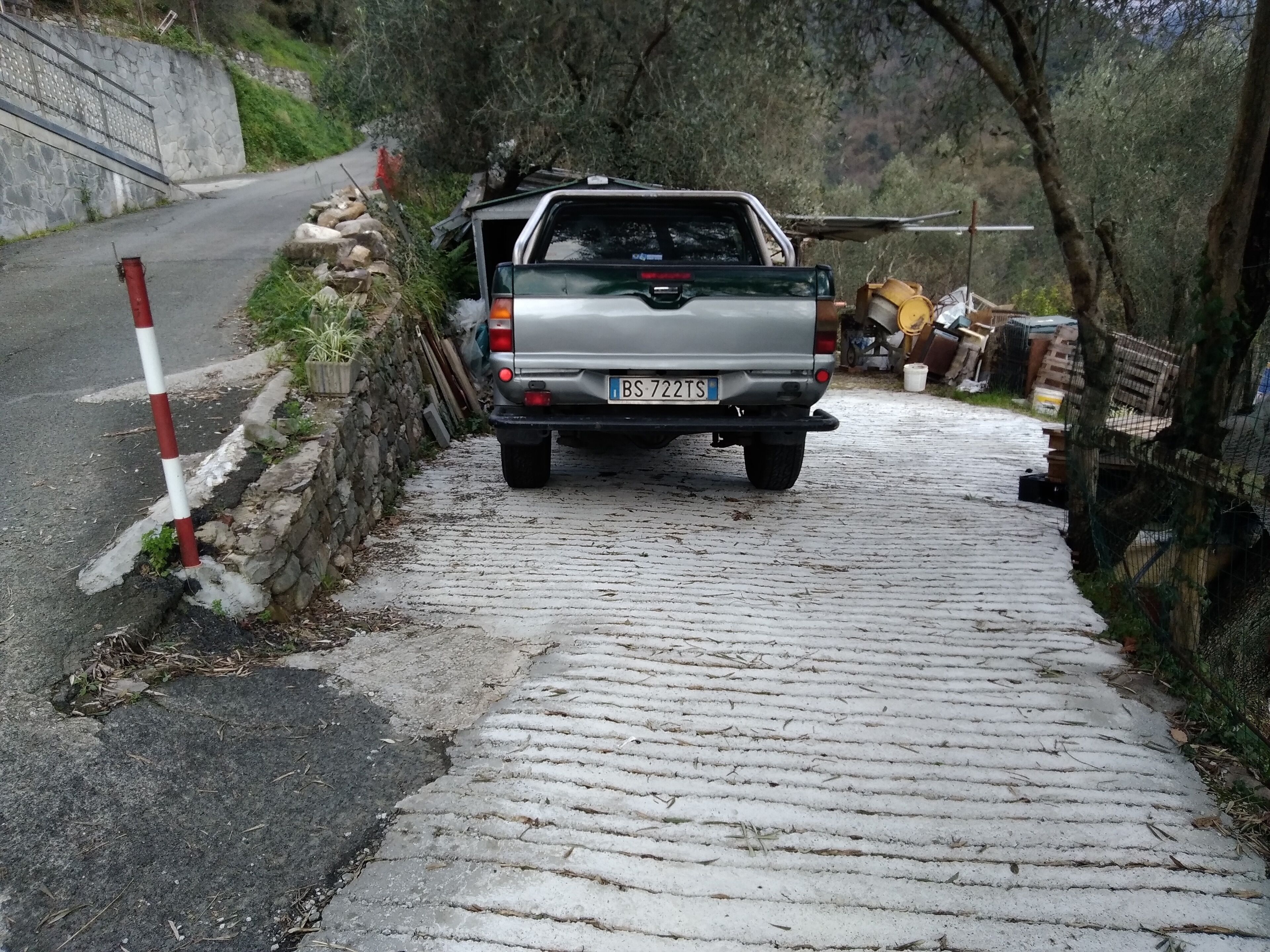 A silver SUV parked on a cobblestone path beside a stone wall.