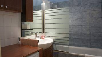 Een moderne badkamer met een houten wastafelmeubel, een witte wasbak, een glazen douchecabine en een bad.