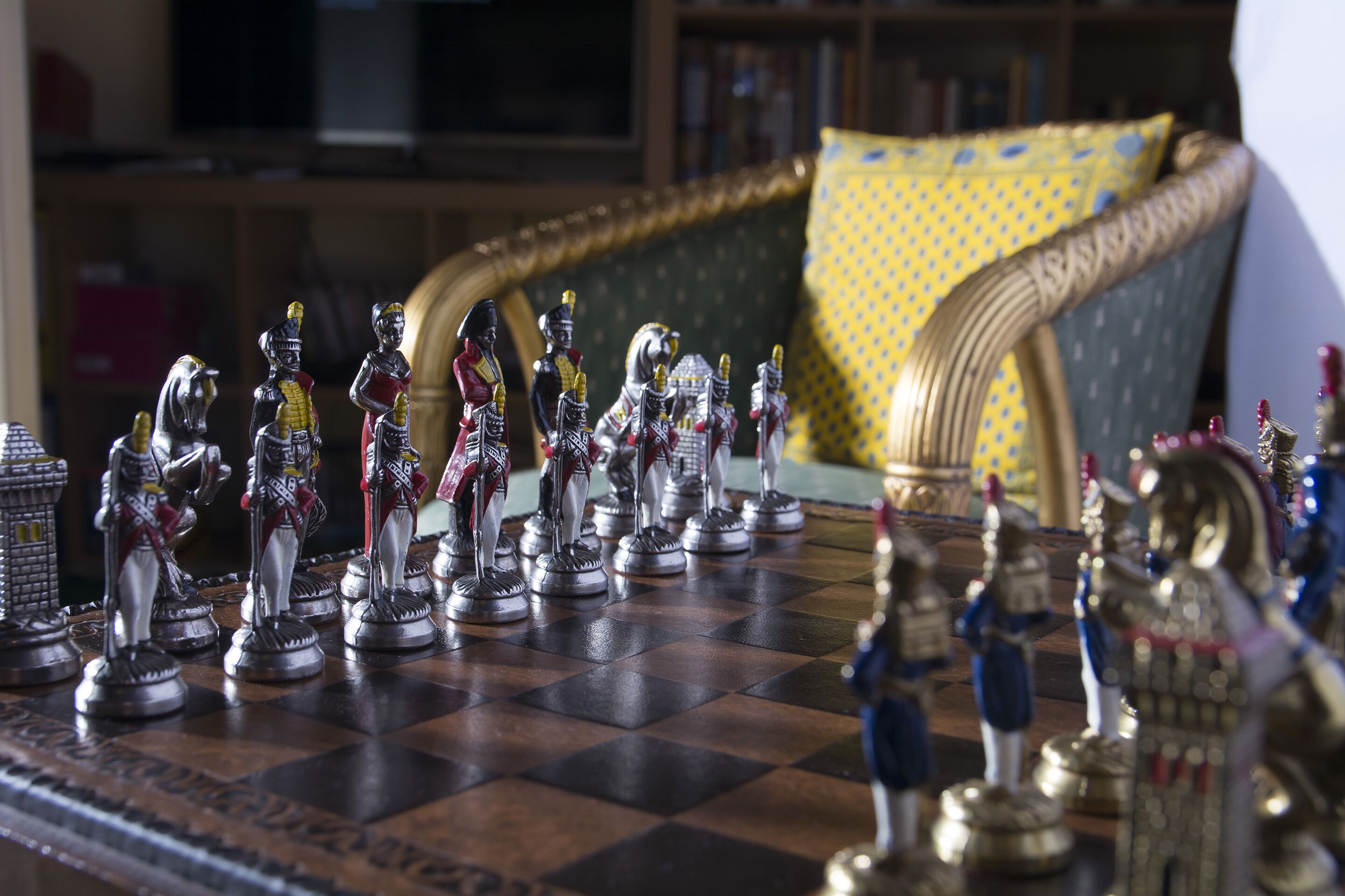 Un tablero de ajedrez con figuras detalladas en una habitación que tiene un sofá y una estantería al fondo.