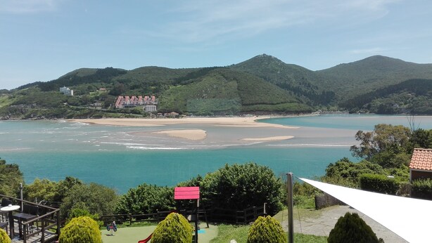A coastal view with a beach, a small pier, and a building with a red roof in the background. - MUNDAKA HOME E-BI 260, With Good Access, Kitchen / Lounge / 2Hab. WIFI, PARKING. (Mundaka)