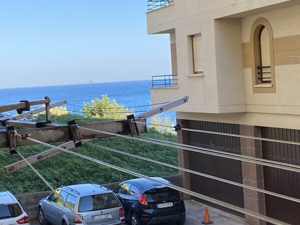 A residential building with a view of the sea, parked cars, and a balcony with a railing.