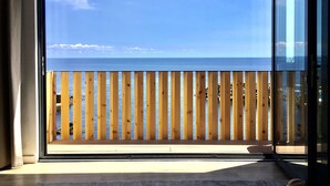 Una habitación con un amplio ventanal que da a una terraza de madera con vista al mar.