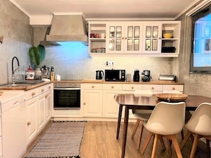 A modern kitchen with white cabinetry, a built-in microwave, a coffee maker, and a dining area with a table and chairs. - Stunning sea front private villa steps away from the sea & natural pools (Lagoa)