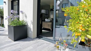 A modern house with a large sliding glass door leading to a living area, a potted plant with purple flowers, and a small tree with orange fruits. - House for 4/5 people, beaches and shops 400 m away (Arradon)