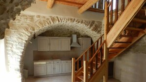 Eine rustikale Küche mit Steinwänden, Holzschränken und einer Holztreppe.