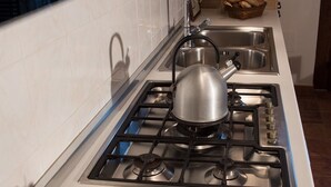 Une cuisine équipée d’une cuisinière à gaz, d’un évier et d’un saladier rempli de fruits posé sur le plan de travail.
