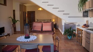 Un salon confortable avec un canapé, une table à manger avec un set de table, un téléviseur et un coin cuisine équipé d’un micro-ondes et d’un panier à fruits.