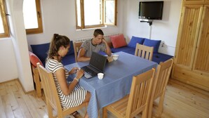 Um quarto com uma mesa de madeira, duas cadeiras, um laptop e uma televisão na parede.