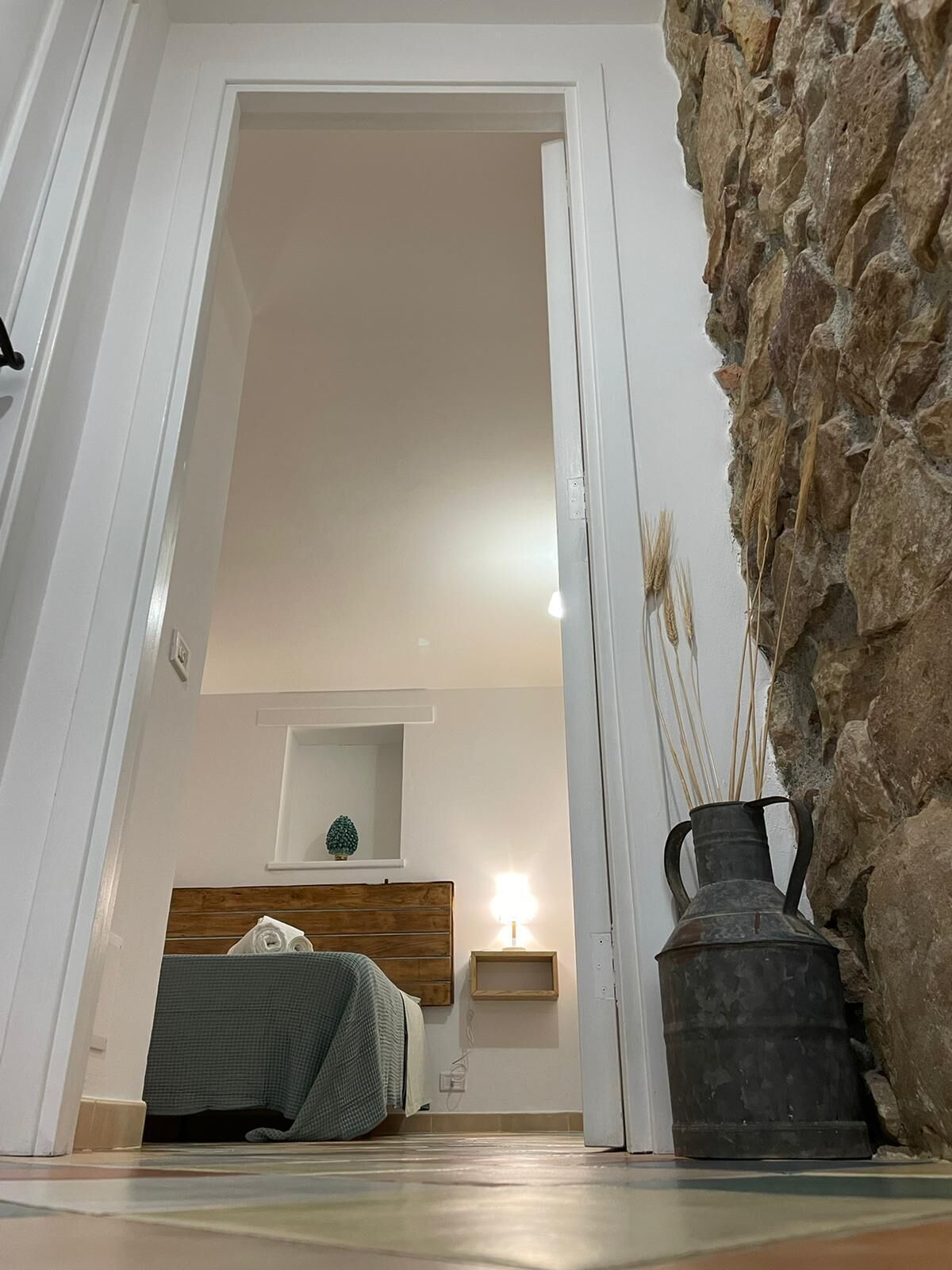 A bedroom with a bed, a bedside table, a lamp, and a stone wall.
