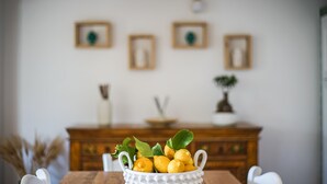 Ein Esstisch mit einer weißen Schüssel Zitronen und Blättern, ein Holzschrank und gerahmte Bilder an der Wand.