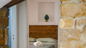 Ein Schlafzimmer mit Schachbrettmuster-Boden, einem Bett mit grüner Bettdecke, einem kleinen Topfpflanzen und einer Steinwand.