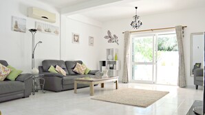A spacious living room with a grey sofa, a coffee table, and a large window with curtains. - Beautiful Spacious Villa in 2,5 Acres A/C Heated Pool Nr Golf & Beaches Sleeps 8 (Budens near VILA DO BISPO)