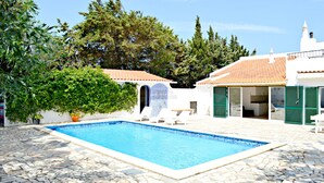 A swimming pool with stone tiles, a white building with green shutters, and a large tree in the background. - Beautiful Spacious Villa in 2,5 Acres A/C Heated Pool Nr Golf & Beaches Sleeps 8 (Budens near VILA DO BISPO)
