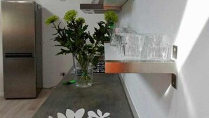 Eine moderne Küche mit einem Edelstahl-Kühlschrank, einer Vase mit Grünpflanzen und einem dekorativen Teller mit Äpfeln auf der Arbeitsfläche.