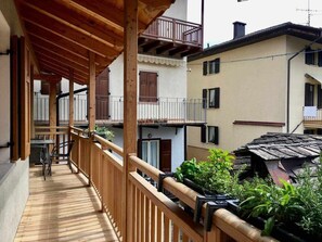 Un balcón de madera con vistas a edificios vecinos y un pequeño jardín.