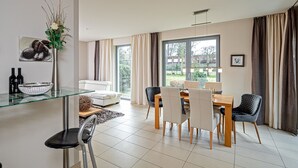 Ett modernt matområde med ett glasbord, fyra stolar och utsikt över omgivningen genom stora fönster.