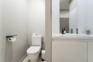 A modern bathroom with a toilet, a toilet paper holder, a sink with a mirror, and a hand soap dispenser.