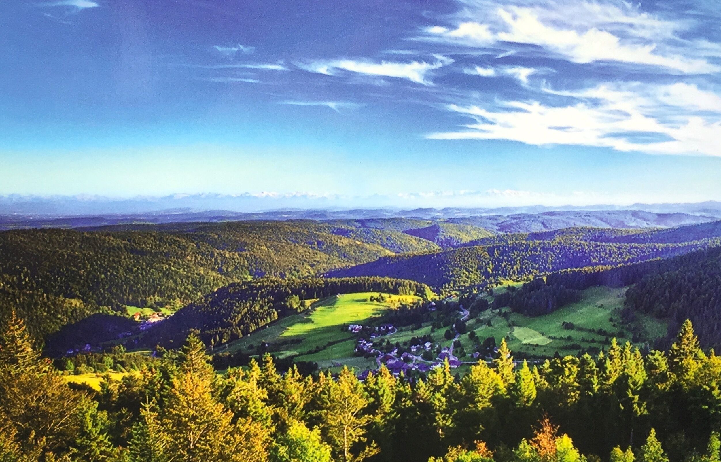 Vista panorámica de un paisaje montañoso con densos bosques y un pequeño pueblo situado en el valle.