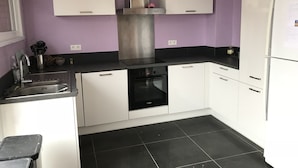 A modern kitchen with white cabinets, a stainless steel range hood, and black countertops. - Leffrinckoucke Plage (Leffrinckoucke)