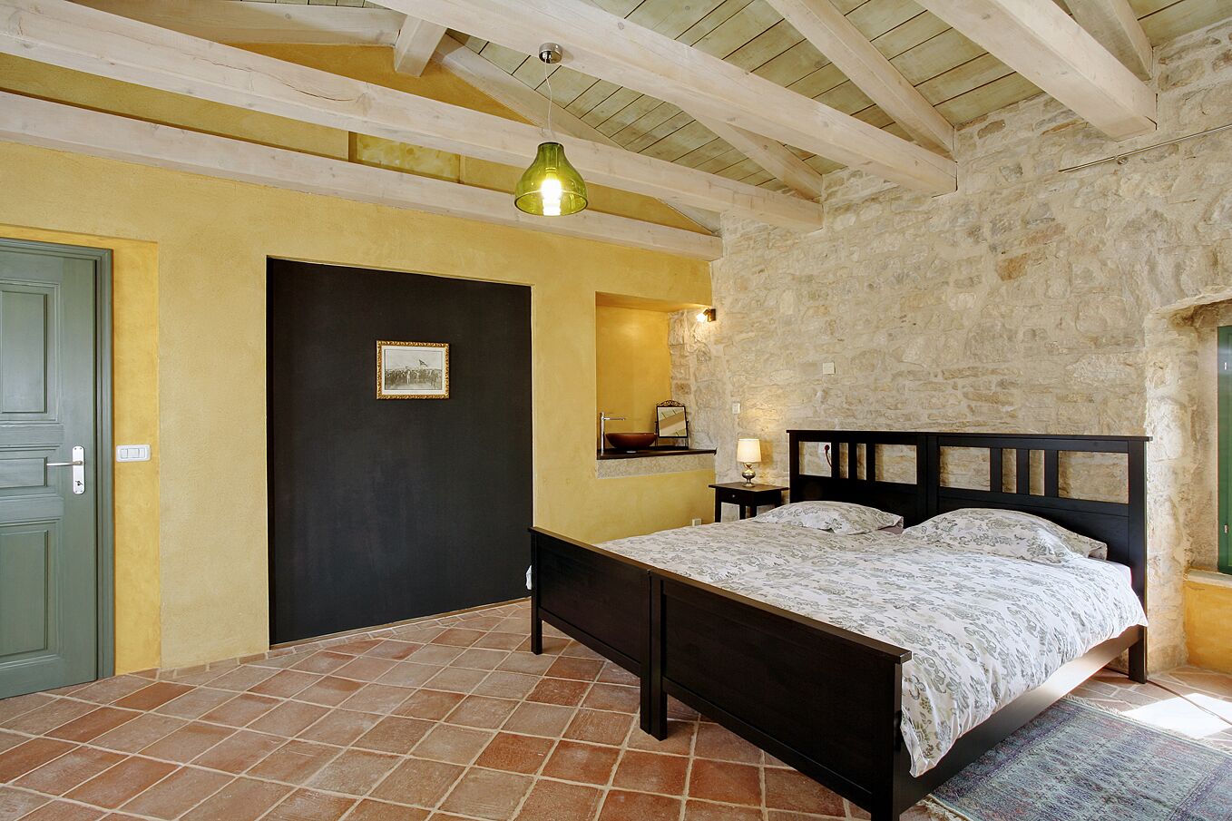 A bedroom with a bed, a door, a stone wall, and a tiled floor.