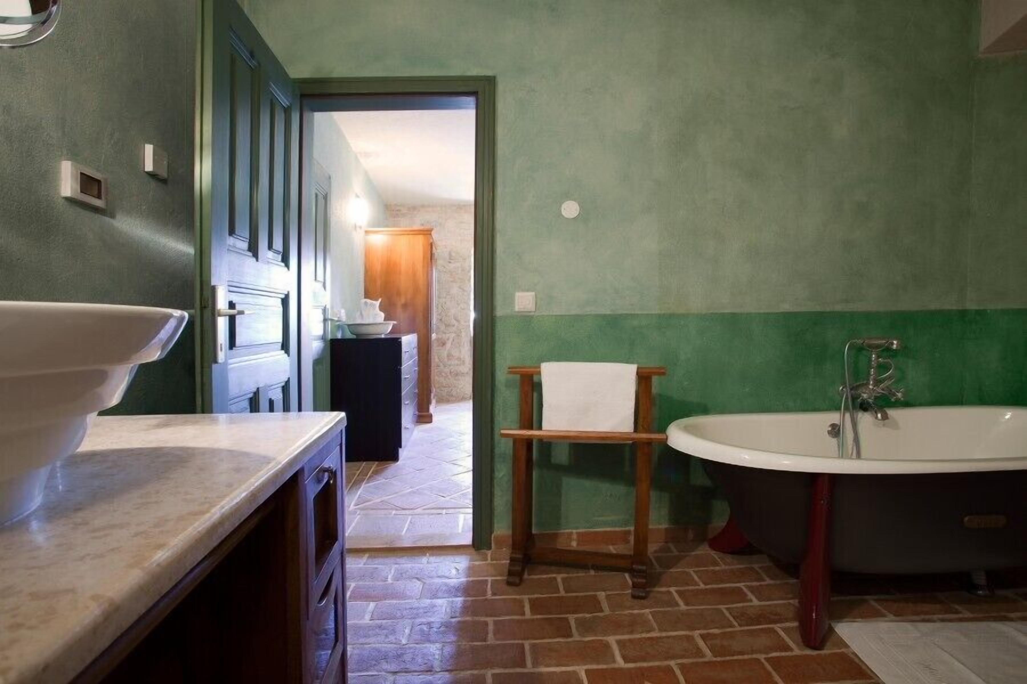 A bathroom with a large sink, a bathtub, and a wooden stool.