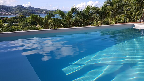 A clear swimming pool with a view of a mountainous landscape and a body of water in the background.