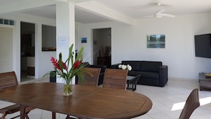 A spacious living area with a wooden dining table, a black sofa, and a ceiling fan.