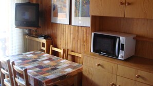 A compact kitchen with wooden cabinets, a microwave, a television, and a table with a quilted tablecloth.