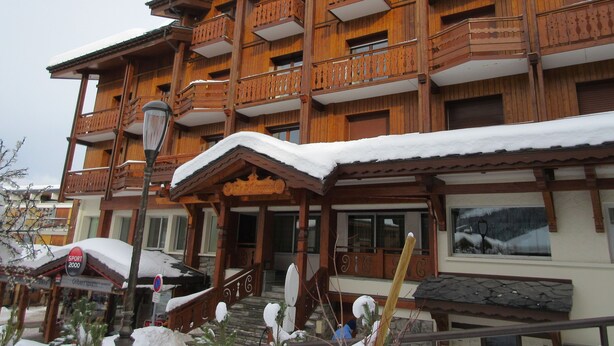 A multi-story wooden building with balconies and a covered entrance.