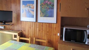 A room with wooden panel walls, a television on a stand, a microwave, a table with a quilt, and two framed pictures.