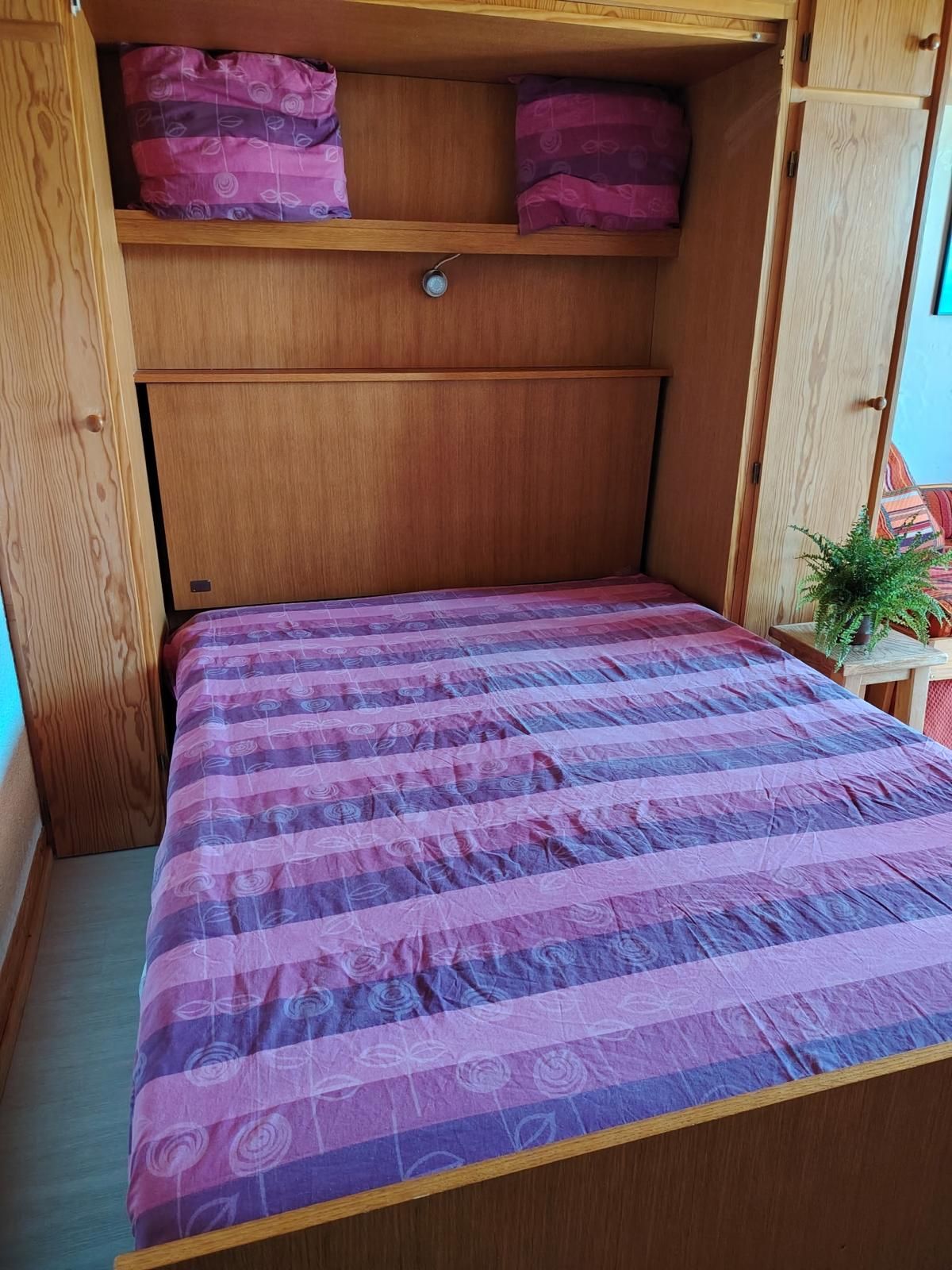 Ein Bett mit gemustertem Überwurf, einem Holz-Kopfteil und einer kleinen Pflanze auf einem Nachttisch.