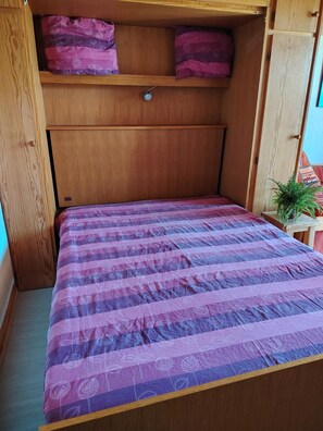 A bed with a patterned bedspread, a wooden headboard, and a small plant on a side table.