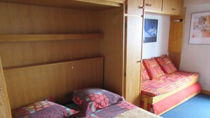 A compact bedroom with a bunk bed and a single bed, wooden walls, and a framed picture on the wall.