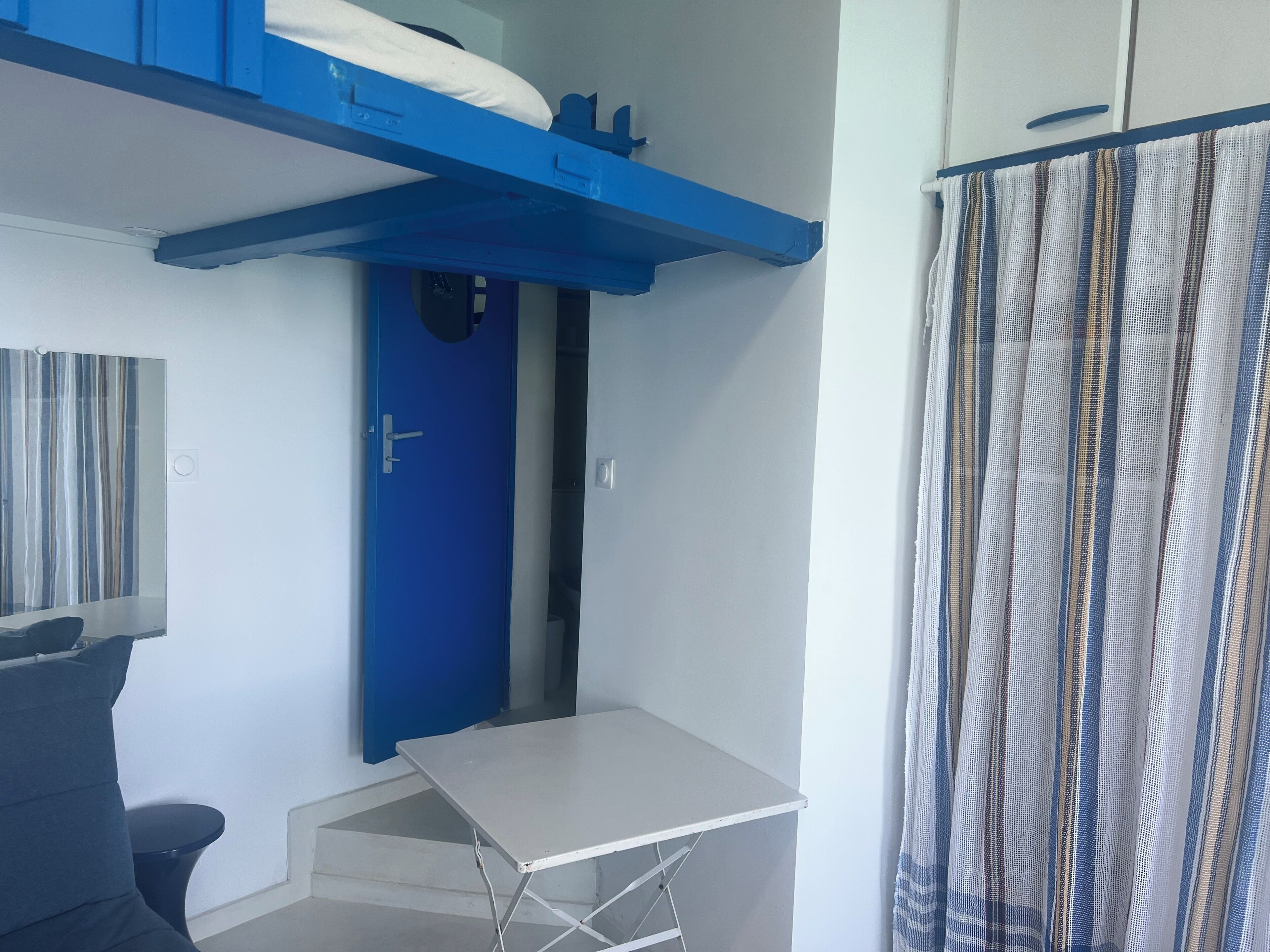A room with a blue door, a white table, a grey sofa, and a striped curtain.