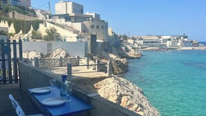 A seaside restaurant with outdoor seating overlooking the ocean, featuring a table set with plates and glasses. - Seafront Cabanon, Access Private to the Sea, Corniche Malmousque! (Marseille)